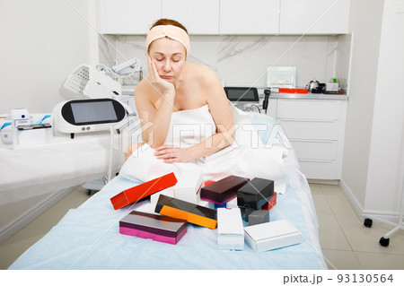Portrait of an elderly woman in a beauty salon. The woman is puzzled by the right choice of cosmetics. 93130564