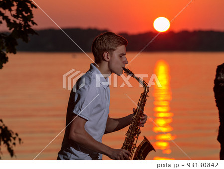 A young guy plays the saxophone in the evening at sunset 93130842