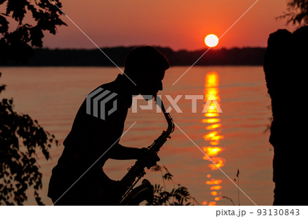 Silhouette of a young guy playing the saxophone in the evening at sunset Silhouette of a young guy playing the saxophone in the evening at sunset 93130843