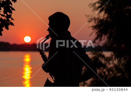 Silhouette of a young guy playing the saxophone in the evening at sunset Silhouette of a young guy playing the saxophone in the evening at sunset 93130844