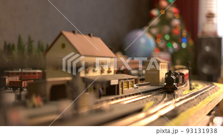 Toy locomotive moving through model train station. Model of vintage train with wagons driving on railroad. Blurred Christmas tree in the background. Toy locomotive moving through model train station. Model of vintage train with wagons driving on railroad. Blurred Christmas tree in the background. 93131938
