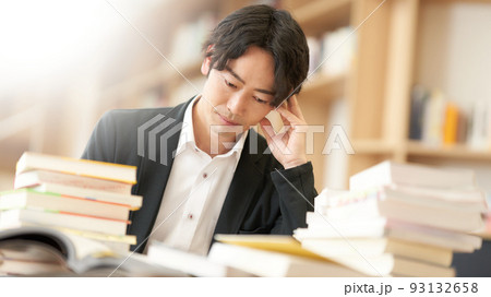 デスクに本を積み重ねながら調べものをする男性 93132658