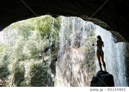 Woman sit on rock under waterfall in tropical jungle 93134902