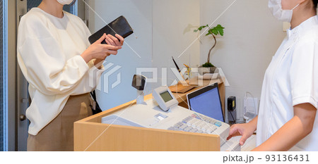 財布を手に持ったマスクを着けた女性が、アクリル板が設置された受付で会計するシーン 財布を手に持ったマスクを着けた女性が、アクリル板が設置された受付で会計するシーン 93136431