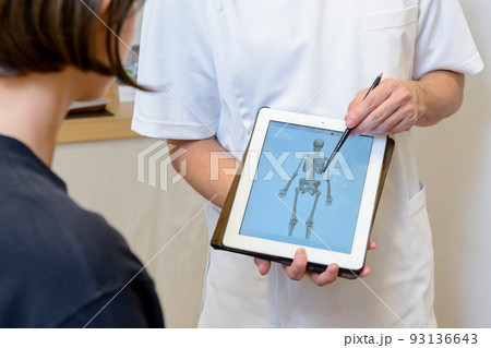 接骨院、整体院、整形外科、クリニックでタブレット画面の人体骨格模型で、患者に説明するシーン	 93136643