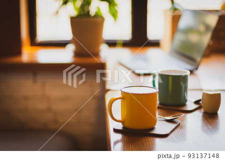 Coffee cups and laptop on the table in cafe. Coffee break. Idyllic place for work. Freelance work place. Morning with coffee and notebook. Cafe interior. Creative space for work. Hot morning drinks. 93137148