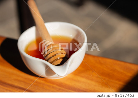Honey with dipper in small white bowl. Homemade honey with wooden stick in sunlight. Honey in jar. Natural sweetener. Healthy nutrition. Natural dessert concept. Sweet food. Honey with dipper in small white bowl. Homemade honey with wooden stick in sunlight. Honey in jar. Natural sweetener. Healthy nutrition. Natural dessert concept. Sweet food. 93137452