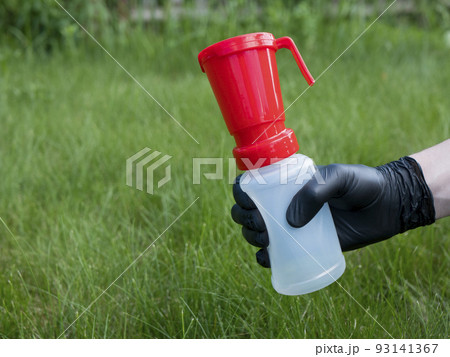 Hand in black nitrile glove holding a teat dip cup for udder cow disinfection on green grass background, copy space. Milking practice 93141367
