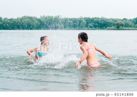 Two cheerful girls splash each other with water in the river. Local tourism. Summer vacation Two cheerful girls splash each other with water in the river. Local tourism. Summer vacation 93141806