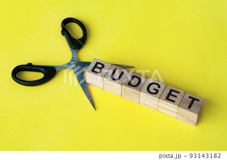 Scissor cutting wooden blocks with text BUDGET. Cutting budget concept. 93143182