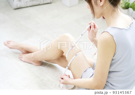自宅でメジャーで太ももを測る女性 自宅でメジャーで太ももを測る女性 93145367