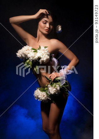 Sensual naked lady with white flowers on body standing in dark studio 93149723
