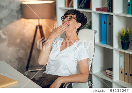 Dark-haired woman in a white shirt sitting in the office and looking tired 93155047