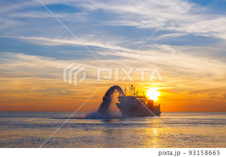 Vessel engaged in dredging at sunset time. Hopper dredger working at sea. Ship excavating material from a water environment. Beautiful sunset, Baltic sea 93158665