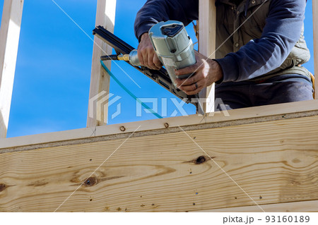 In this case, the builder uses an air hammer when nailing wooden beams for construction in the housing development. 93160189