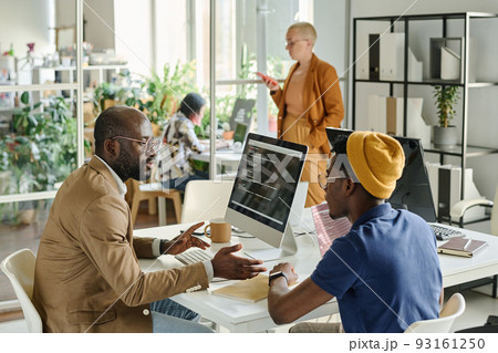 African programmers discussing software together while sitting at table with computer during meeting African programmers discussing software together while sitting at table with computer during meeting 93161250