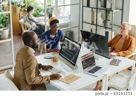 High angle view of programmers developing new software on computers together at table at meeting 93161251