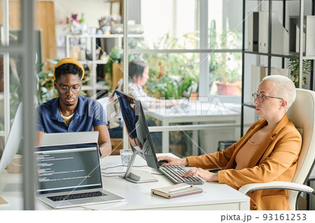 Colleagues working with software on computers sitting at table at modern office Colleagues working with software on computers sitting at table at modern office 93161253