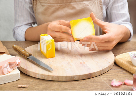 Woman holding natural handmade soap at wooden table, closeup 93162235