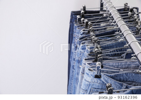 Rack with different jeans on light background, closeup. Space for text Rack with different jeans on light background, closeup. Space for text 93162396