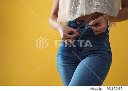 Woman unzipping jeans on yellow background, closeup. Space for text 93162424