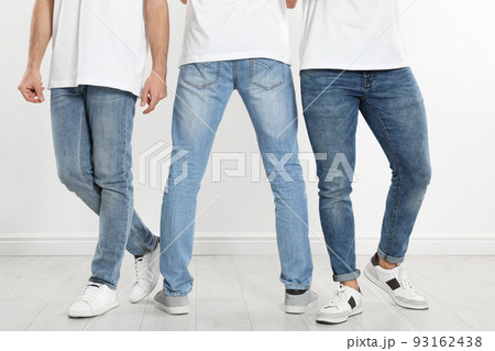 Group of young men in stylish jeans near white wall, closeup 93162438