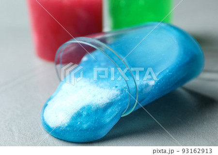 Overturned plastic container with light blue slime on grey background, closeup 93162913