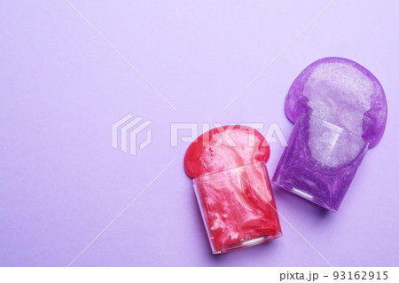 Overturned plastic containers with bright slimes on violet background, top view. Space for text 93162915
