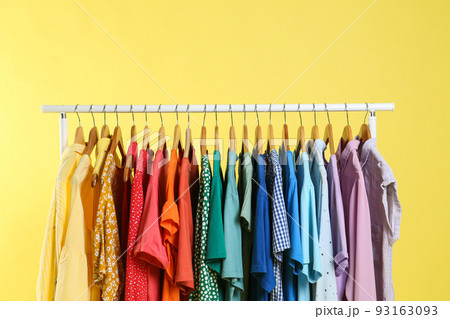 Bright clothes hanging on rack against yellow background. Rainbow colors 93163093