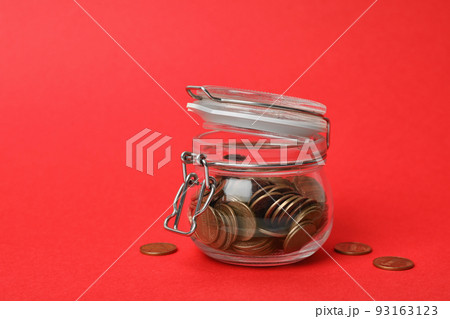Glass jar with coins on red background 93163123
