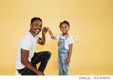 Smiling african dad and his daughter girl in casual clothes posing isolated on yellow background Smiling african dad and his daughter girl in casual clothes posing isolated on yellow background 93164605