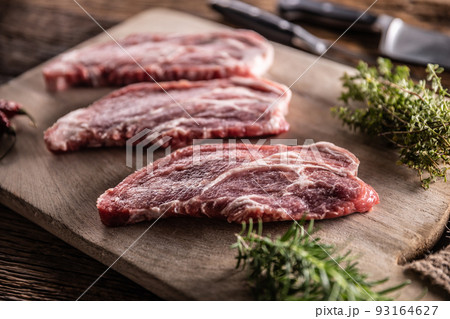 Raw pork neck cut on a cutting board with rosemary and thyme herbs Raw pork neck cut on a cutting board with rosemary and thyme herbs 93164627