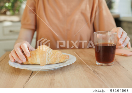 woman drinks coffee in the kitchen and eats a croissant for breakfast. a beautiful European woman enjoys life in the morning woman drinks coffee in the kitchen and eats a croissant for breakfast. a beautiful European woman enjoys life in the morning 93164663