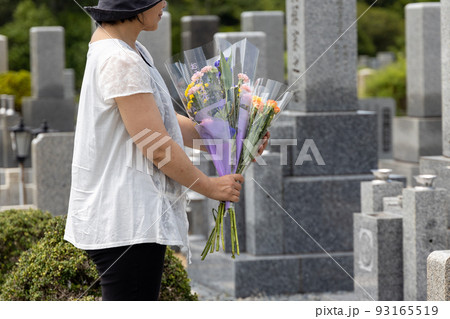 お墓詣りの時にきれいなお花をお墓にお供えしようとしている中高年女性 お墓詣りの時にきれいなお花をお墓にお供えしようとしている中高年女性 93165519