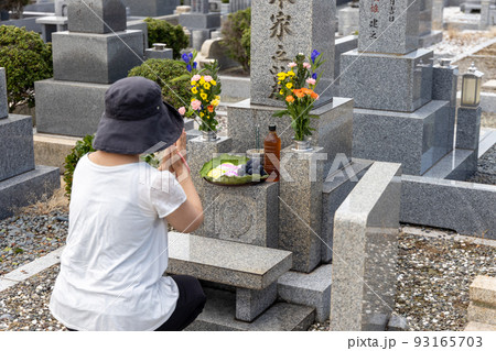 お墓参りに来てきれいなお花とお供え物をして手を合わせている中年女性 93165703
