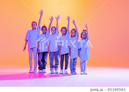 Dance group of happy, active little girls in t-shirts and jeans in action isolated on orange background in neon. Concept of music, fashion, art, childhood Dance group of happy, active little girls in t-shirts and jeans in action isolated on orange background in neon. Concept of music, fashion, art, childhood 93169561