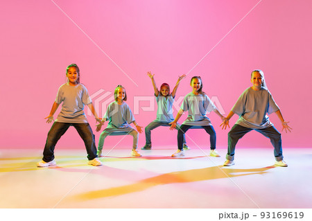 Portrait of cheerful, active little girls, happy kids dancing isolated on orange background in neon light. Concept of music, fashion, art, childhood, hobby 93169619