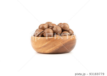 Wooden bowl full of macadamia nuts on a white background. 93169779