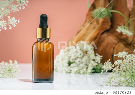 Amber glass dropper bottle of serum or oil in nature. Leaves and flowers on pink Amber glass dropper bottle of serum or oil in nature. Leaves and flowers on pink 93170323