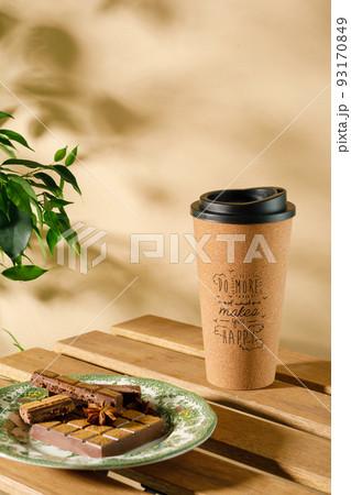 A takeaway coffee cup made of cork wood with a positive inscription on the table on a beige-brown background and a plate with chocolate and spices 93170849