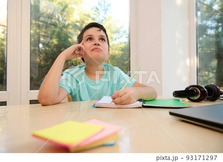 Handsome pensive Caucasian child, smart schoolboy thoughtfully looking up while solving examples, doing homework at home. New academic year semester. Back to school. Homeschooling and online education Handsome pensive Caucasian child, smart schoolboy thoughtfully looking up while solving examples, doing homework at home. New academic year semester. Back to school. Homeschooling and online education 93171297
