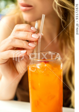 Young woman drinks fruit cocktail or freshly squeezed juice or refreshing drink and holds sipping straw with her fingers Young woman drinks fruit cocktail or freshly squeezed juice or refreshing drink and holds sipping straw with her fingers 93172876