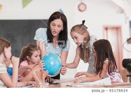 Female teacher with kids in geography class looking at globe. Side view of group of diverse happy school kids with globe in classroom at school. Female teacher with kids in geography class looking at globe. Side view of group of diverse happy school kids with globe in classroom at school. 93176634