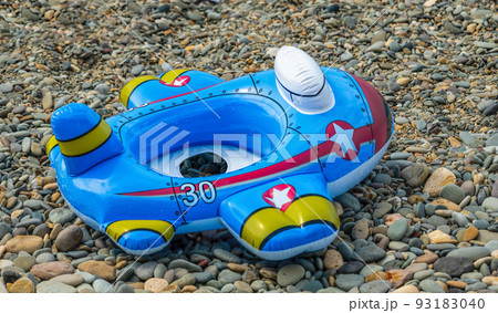 Bright children's inflatable circle lying on the ground on the pebbles beach. Lifebuoy blue in the shape of a airplane Bright children's inflatable circle lying on the ground on the pebbles beach. Lifebuoy blue in the shape of a airplane 93183040