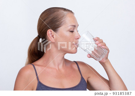 Woman of 40s holding glass of pure water and drinking 93185387