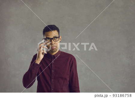 Confused young black man holding mobile phone, making call and waiting for answer 93186758