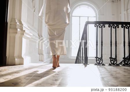 A girl in a wedding dress walks barefoot in a bright hall A girl in a wedding dress walks barefoot in a bright hall 93188200