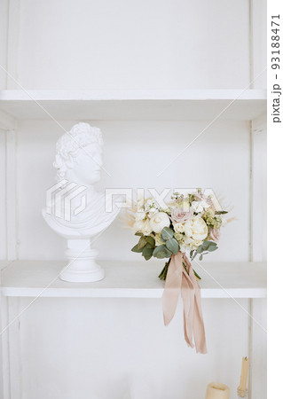 The wedding bouquet is on a white shelf next to a plaster sculpture The wedding bouquet is on a white shelf next to a plaster sculpture 93188471