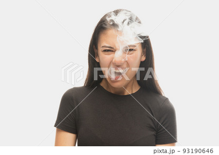 Angry young girl with dark hair releases smoke from the mouth isolated over white background. Concept of mental health, art, human emotions 93190646