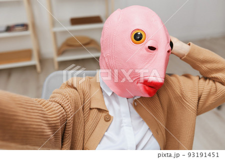 Funny blonde lady in pink fish mask warm sweater doing selfie use phone sitting in armchair at modern home interior. Pause from work, take a break, social media in free time concept. Wide angle 93191451